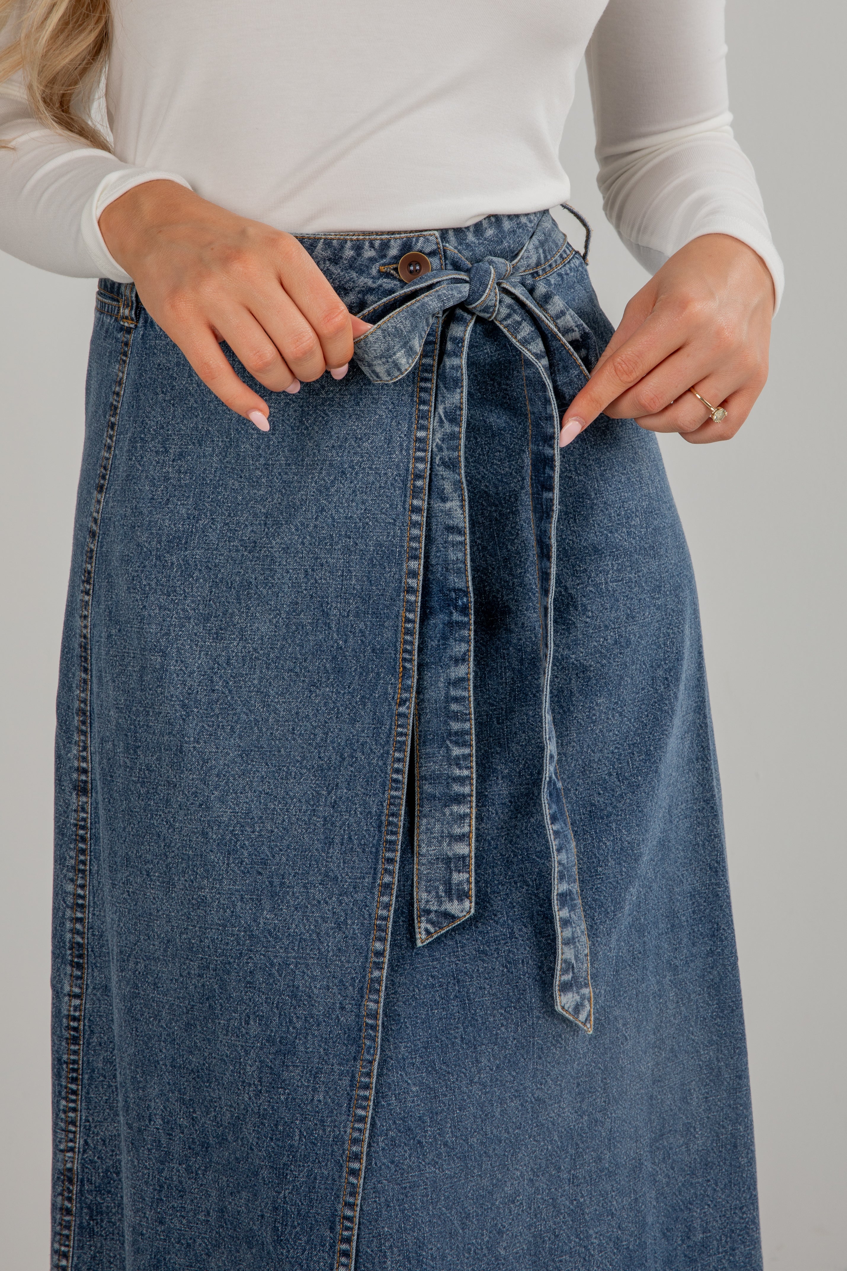 Person wearing a blue denim skirt with a white top on a plain background