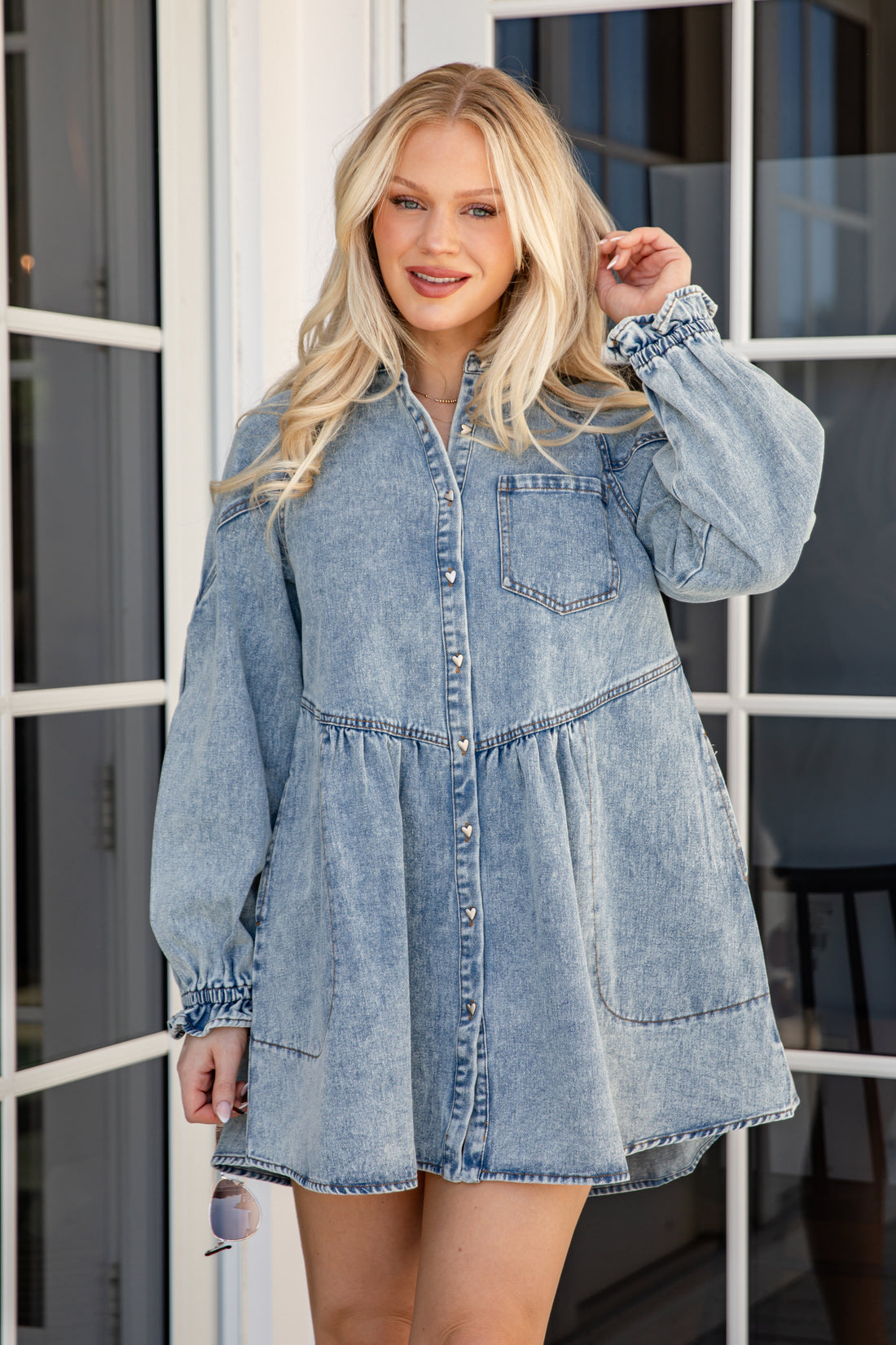 Woman wearing a denim dress standing in front of a glass door.