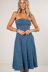 A woman modeling a strapless blue denim dress with a fitted corset-style bodice and a flared skirt, photographed against a plain light studio background.