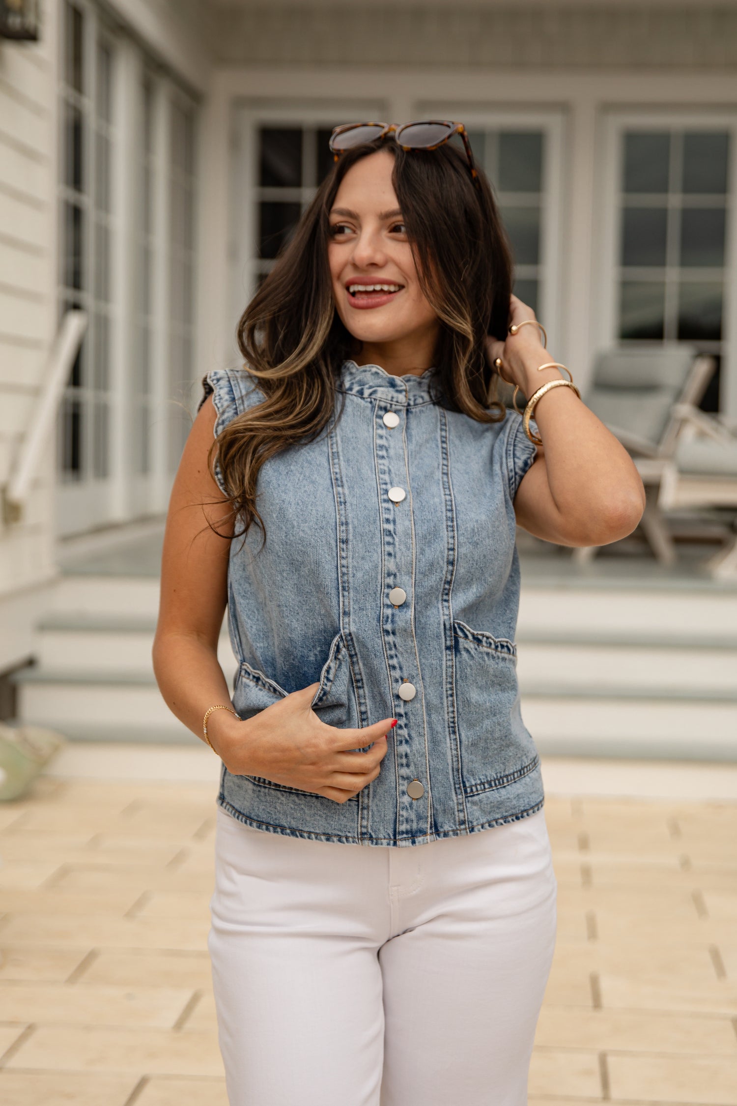Woman wearing a denim vest and white pants standing on a patio.