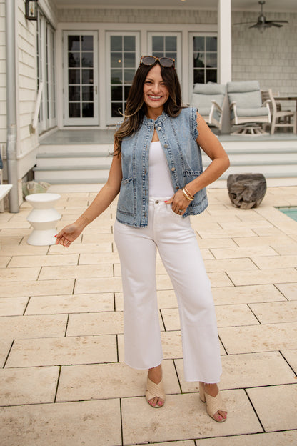 Woman in a denim vest and white pants standing on a patio.