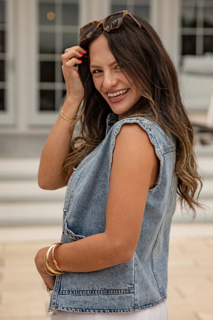 Woman wearing a denim vest and sunglasses, standing outdoors.