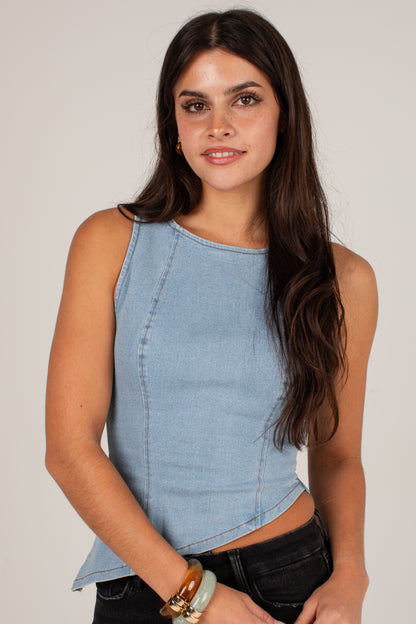 A woman wearing a light blue sleeveless cropped top with a curved hem, paired with black jeans, against a plain light gray studio background.