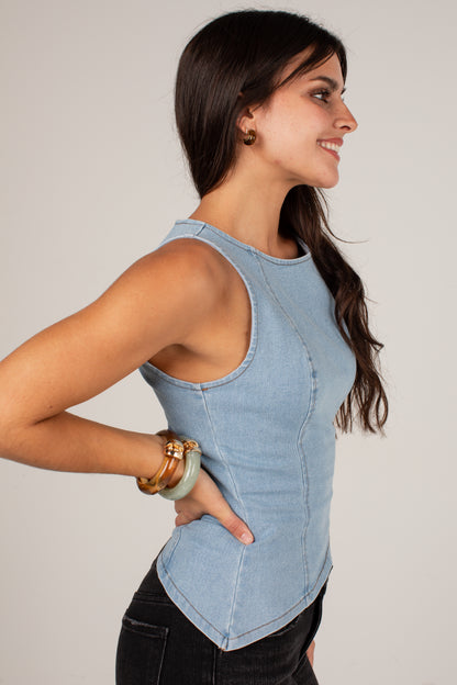 A woman wearing a light blue denim sleeveless top, shown in profile against a plain light gray studio background.