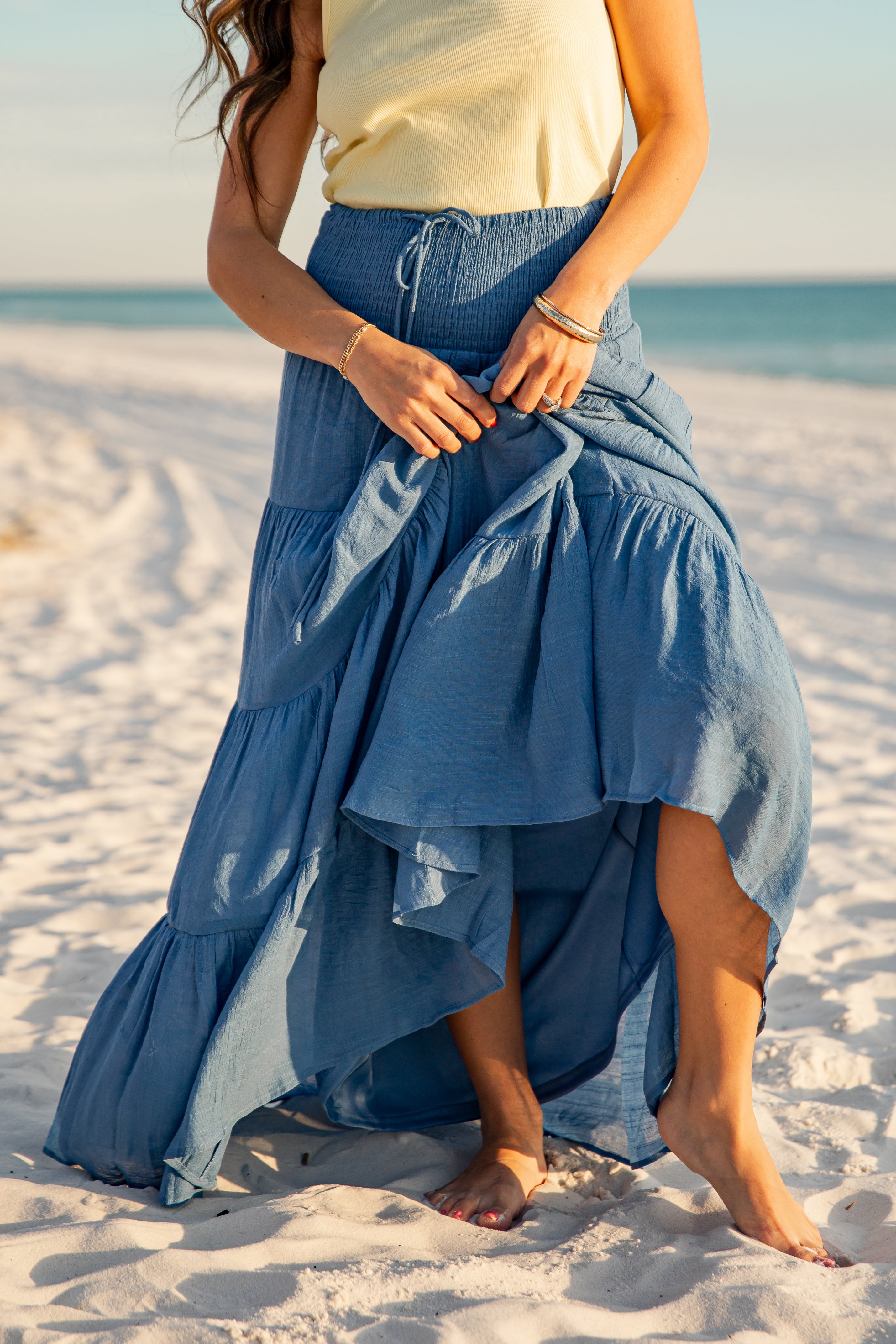 Woman in a blue denim skirt standing on a sandy beach.