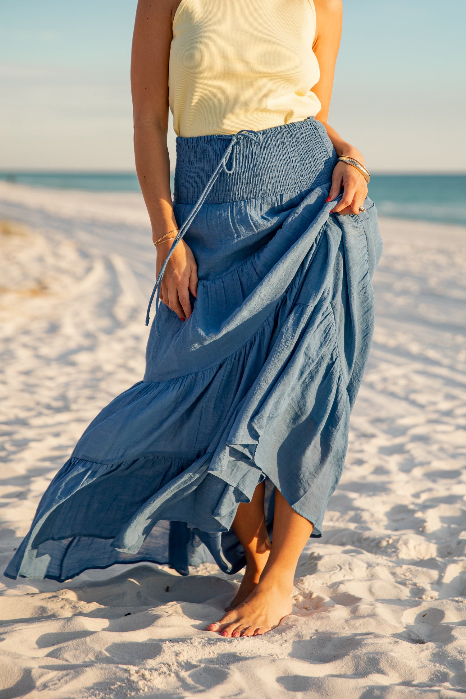 Person wearing a blue skirt on a sandy beach with ocean view