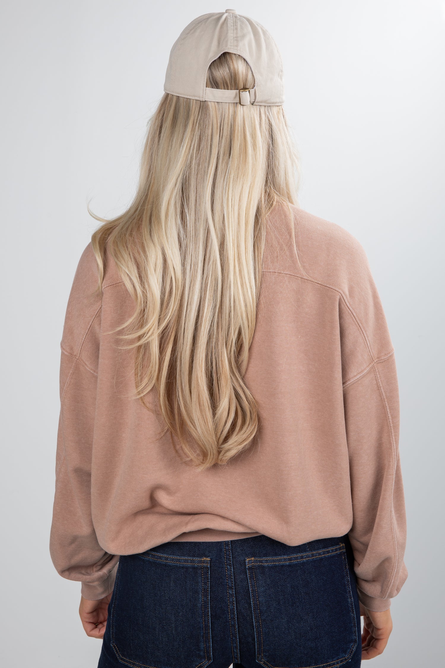 Person wearing a beige cap and oversized beige sweatshirt with blue jeans on a white background