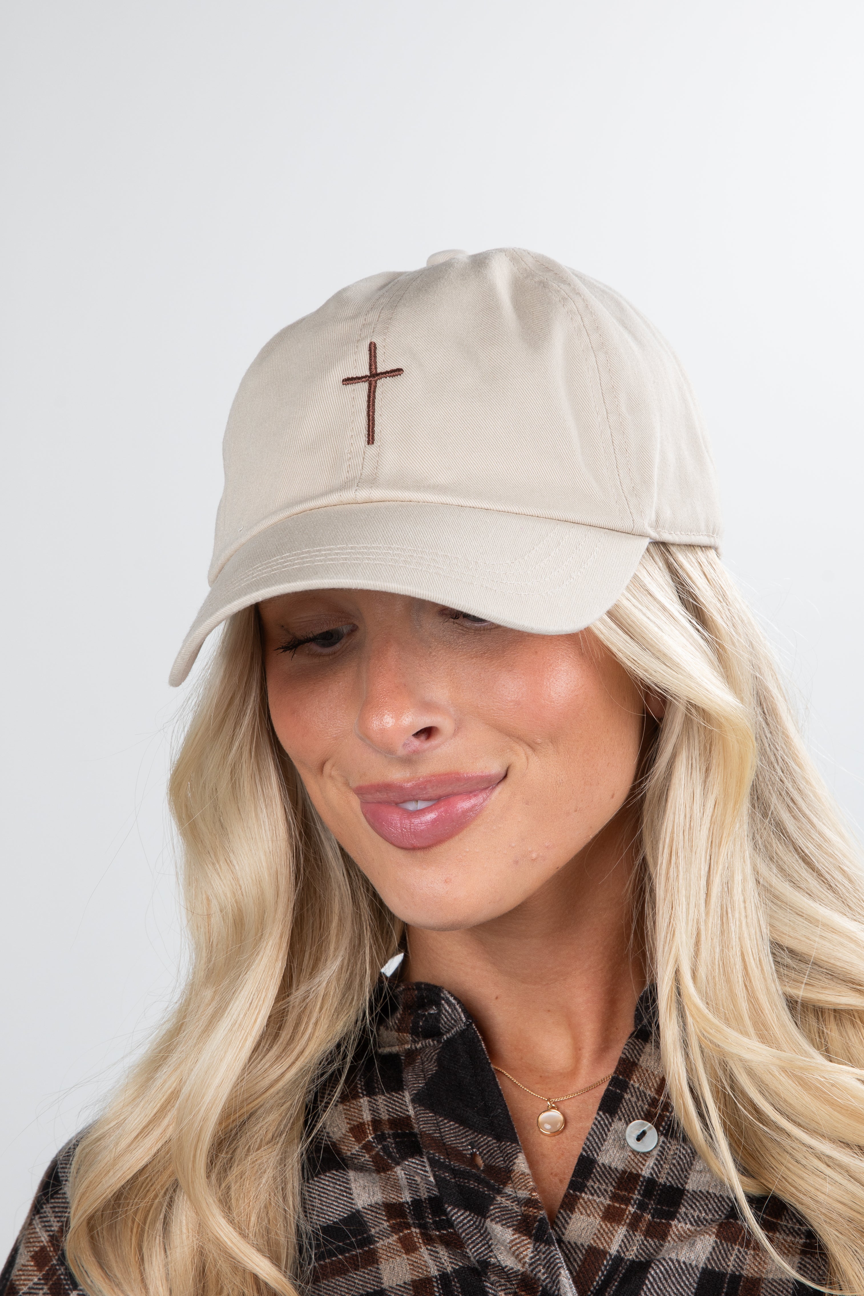 Woman wearing a beige cap with a cross emblem on a plain background
