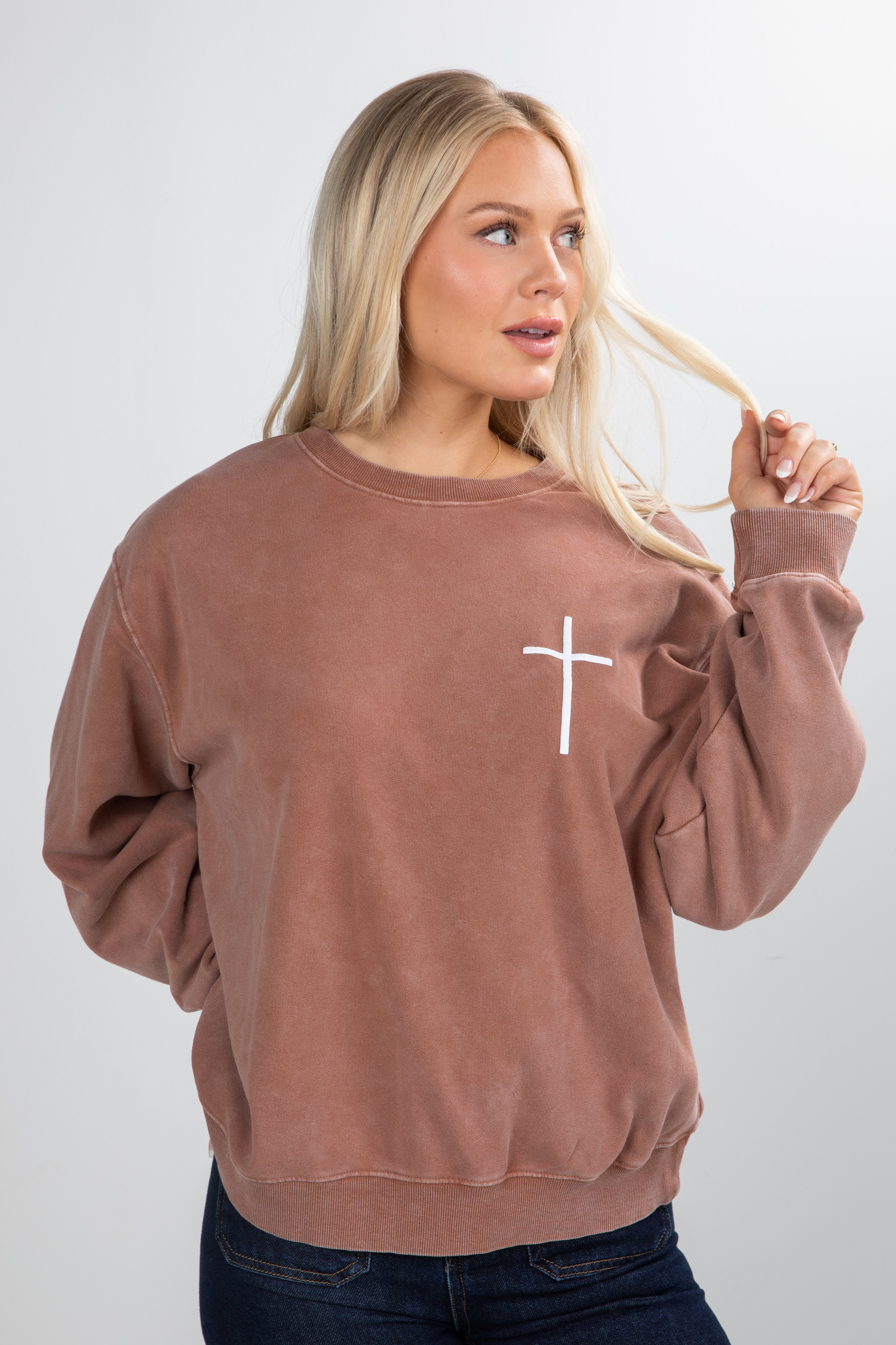 Woman wearing a brown sweatshirt with a white cross design on a plain background