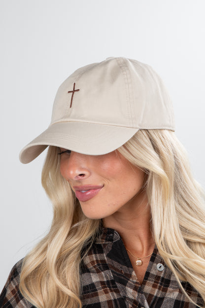 Woman wearing a beige cap with a cross emblem on a plain background