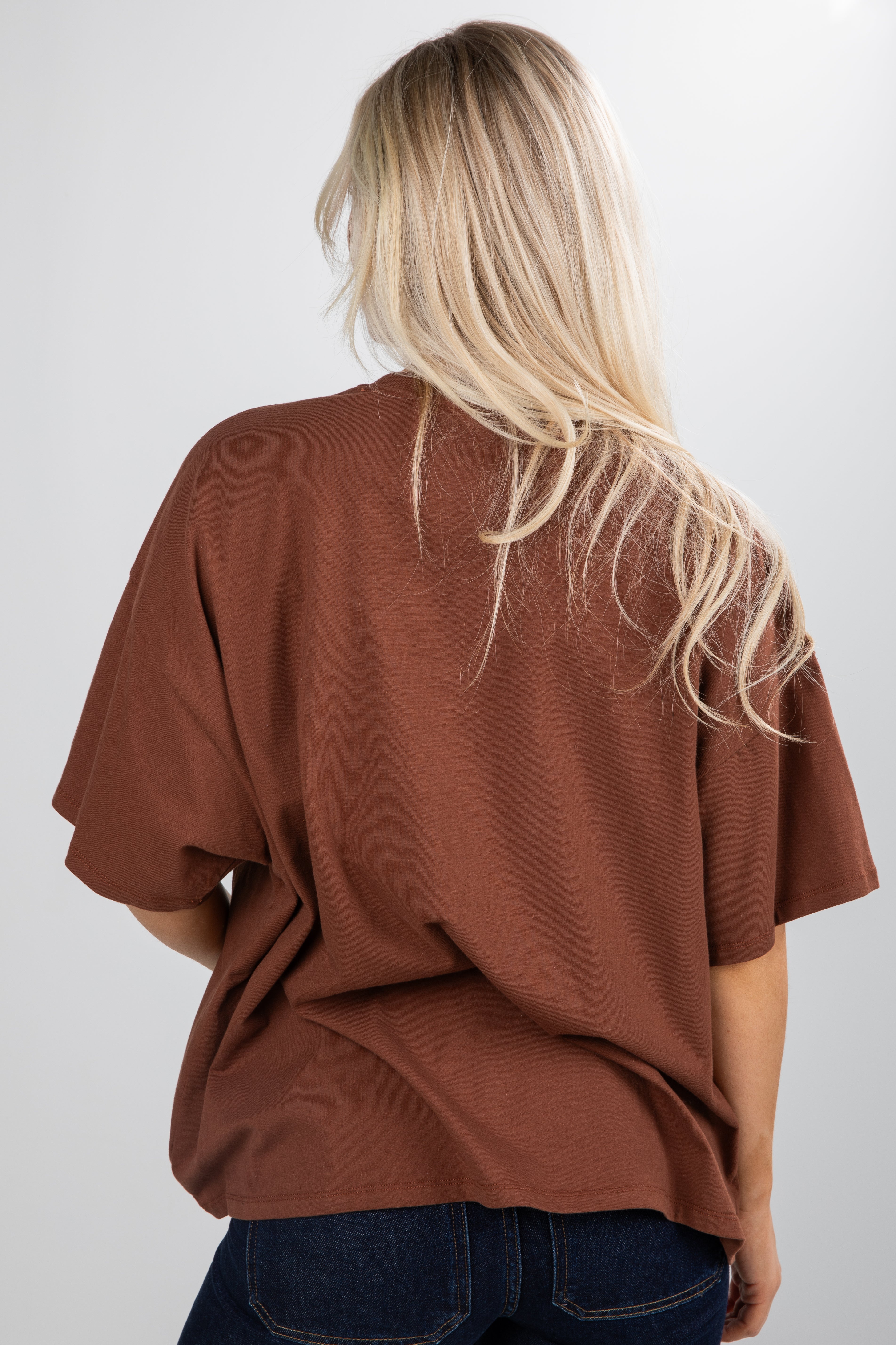 Person wearing a brown oversized shirt and blue jeans on a white background