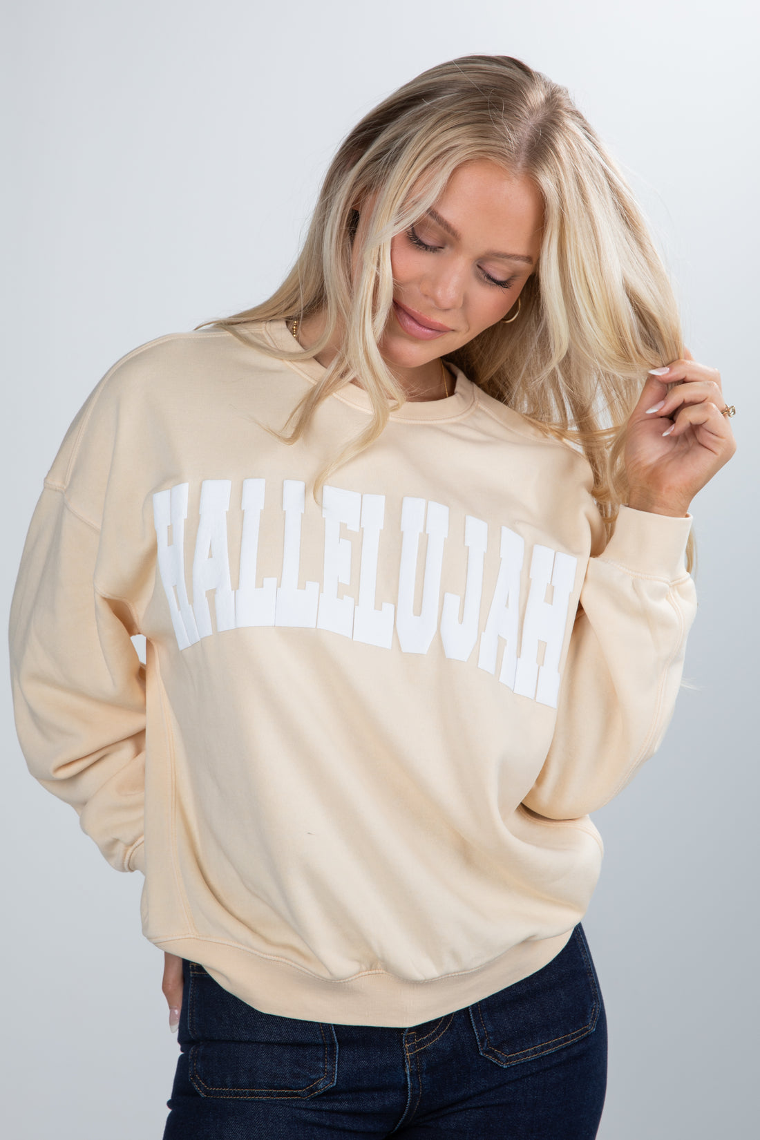 Woman wearing a beige sweatshirt with text, posing against a plain background