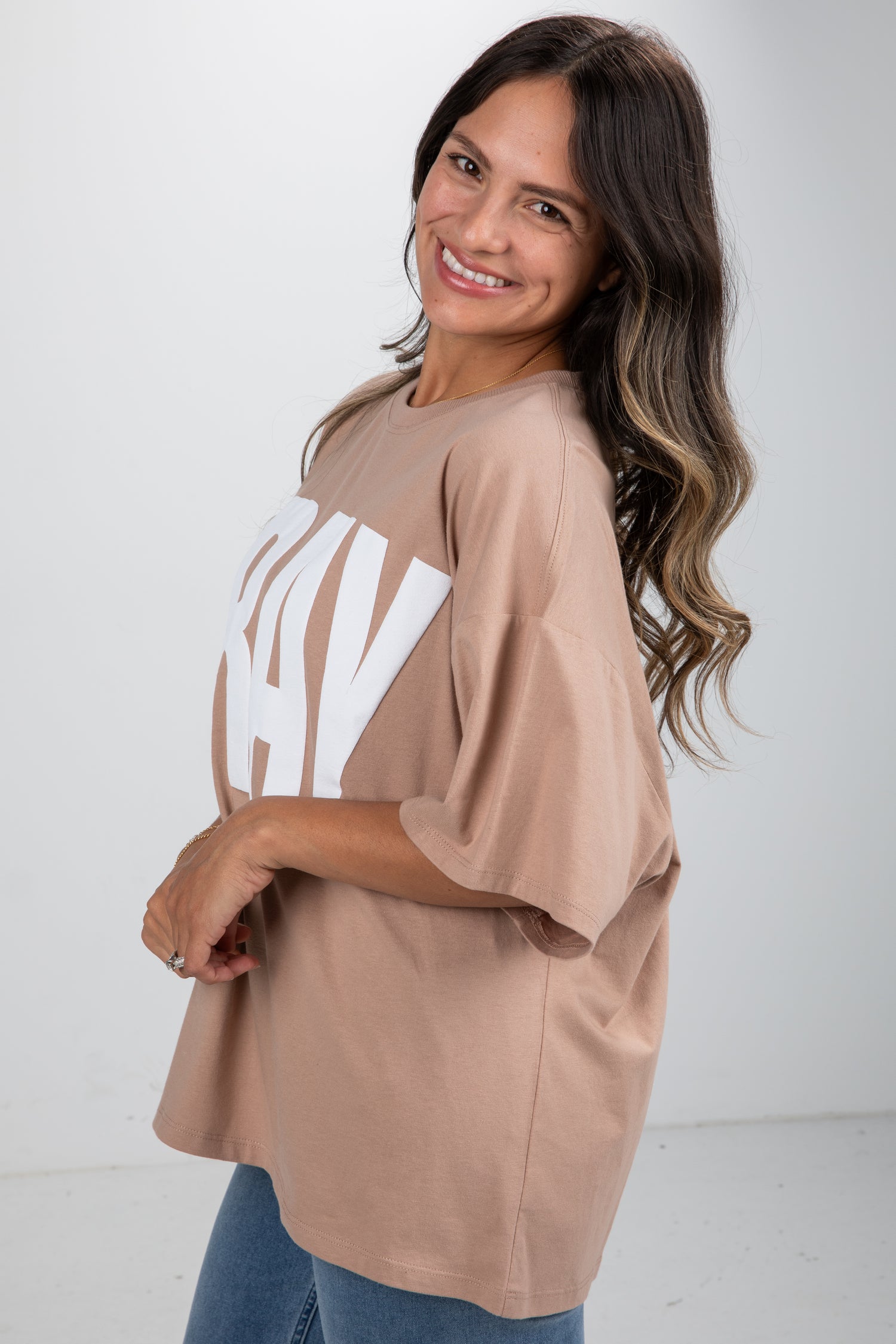 Woman wearing a beige oversized t-shirt with a logo on a white background