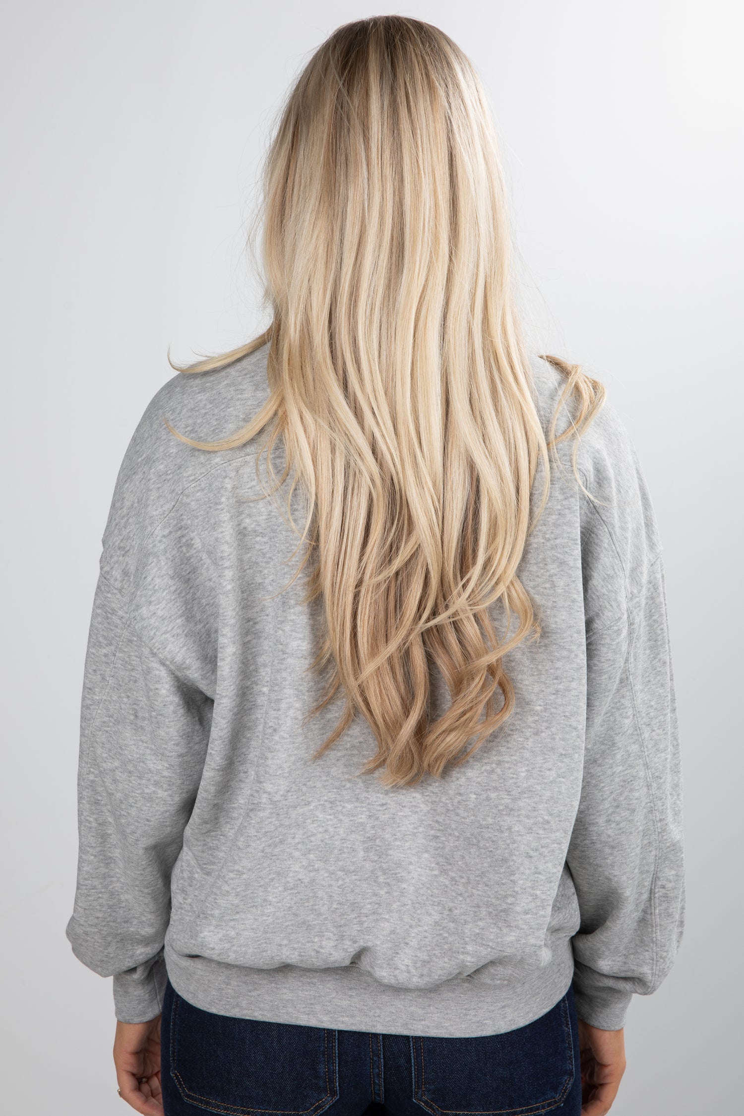 Person wearing a gray hoodie with long blonde hair, standing against a plain background
