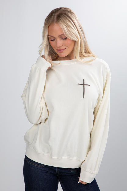 Woman wearing a white sweatshirt with a cross design on a plain background