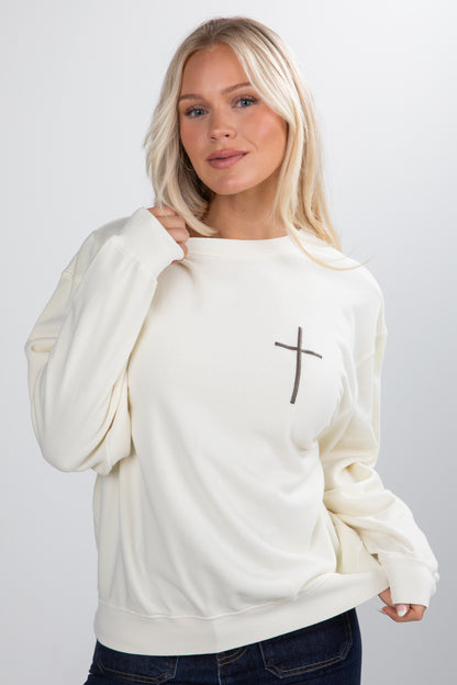 Woman wearing a white sweatshirt with a cross design on a plain background