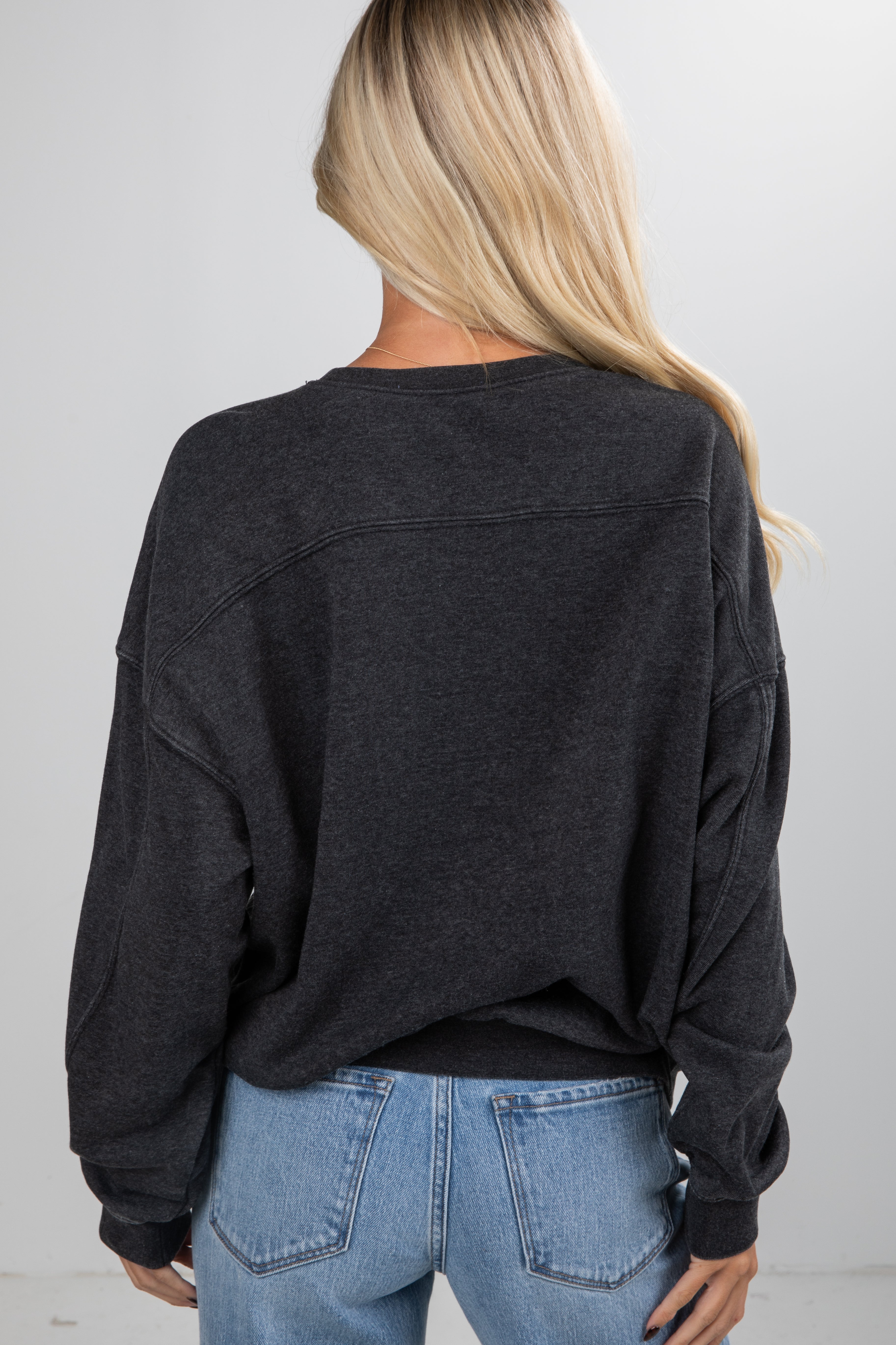Person wearing a black oversized sweater and blue jeans against a plain background