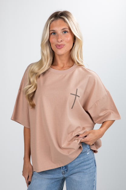 Woman wearing a beige oversized t-shirt with a black cross design on a plain background