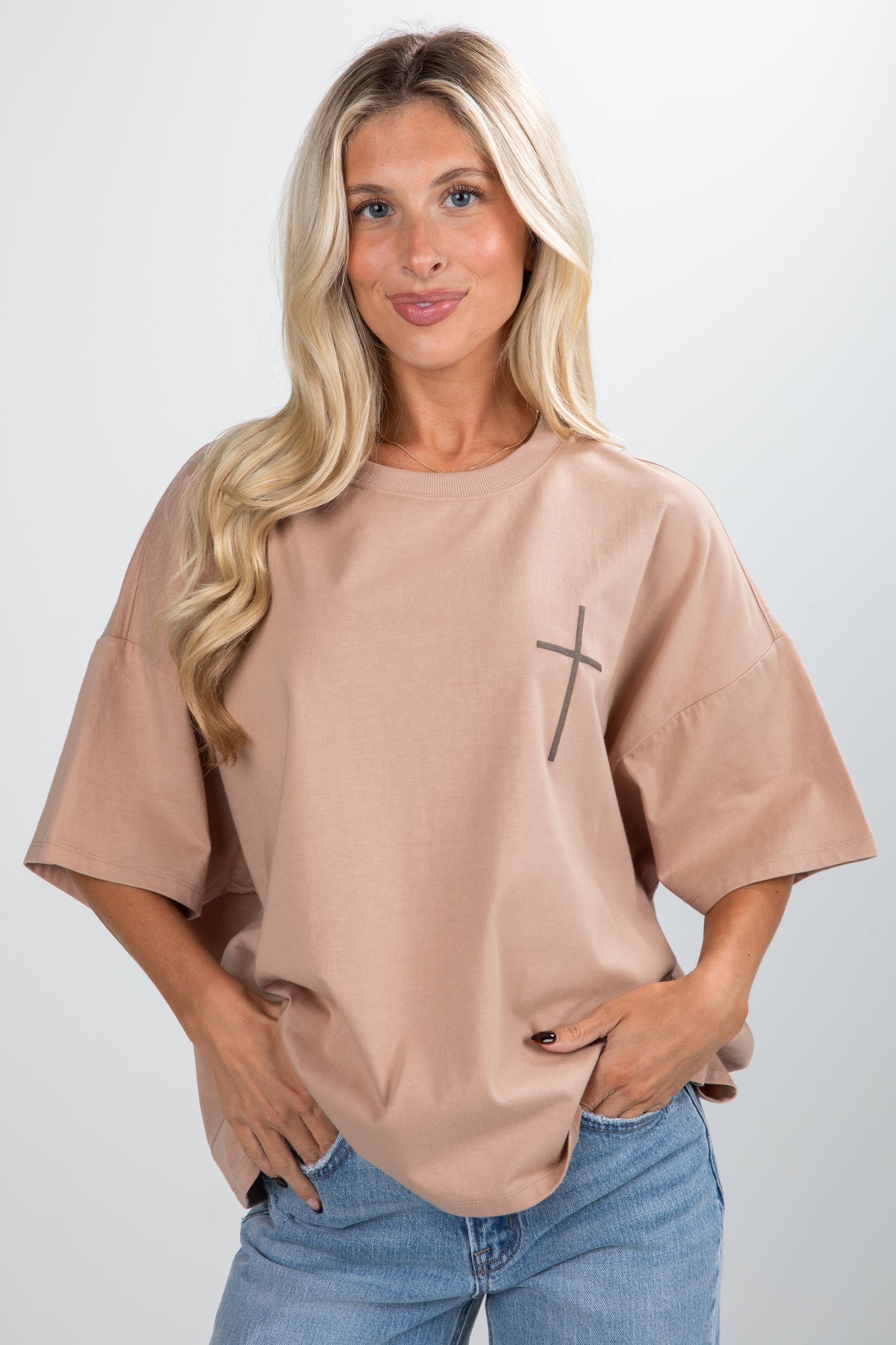Woman wearing a beige t-shirt with a black cross design on a plain background
