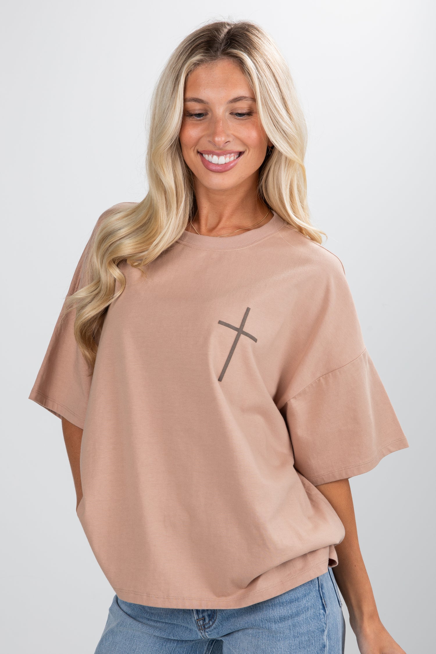Woman wearing a beige t-shirt with a black cross design on a white background
