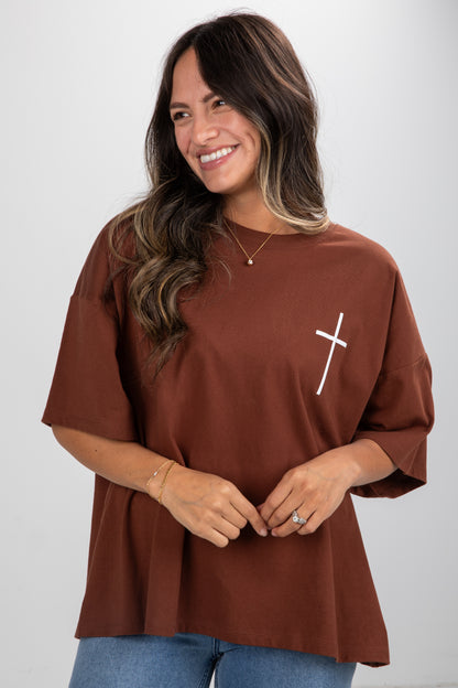 Woman wearing a brown top with a white cross design on a plain background