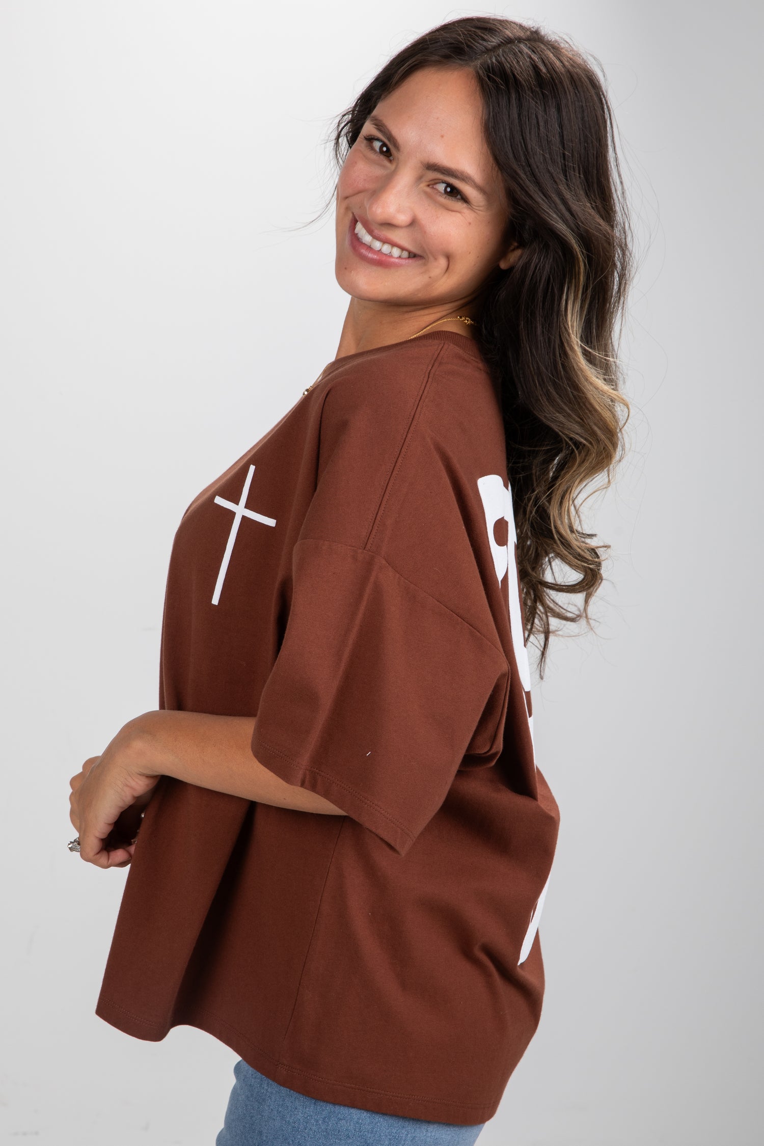 Woman wearing a brown oversized shirt with white designs on a plain background