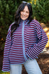 A woman smiling outdoors wearing a red and blue horizontally striped zip-up fleece jacket with a light blue zipper, paired with light-wash jeans.