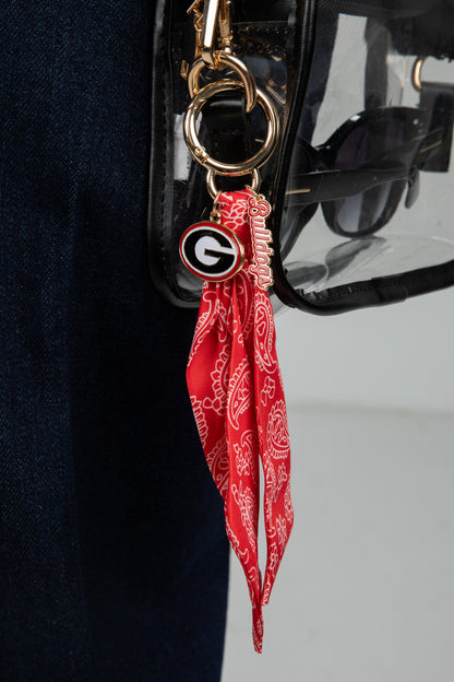 Red bandana keychain with a logo attached to a black handbag.