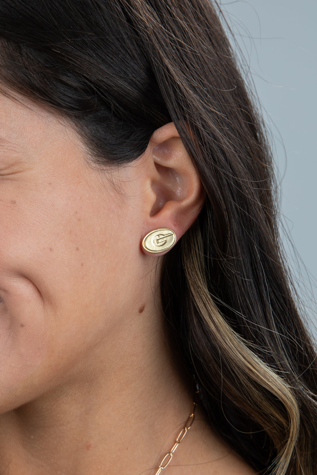 Close-up of a person wearing a gold earring with a leaf design on a neutral background