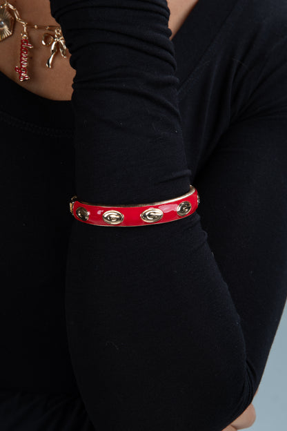 Red leather bracelet with gold accents on a person wearing a black long-sleeve shirt.