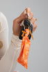 Hand holding a keychain with an orange bandana and gold ring against a gray background