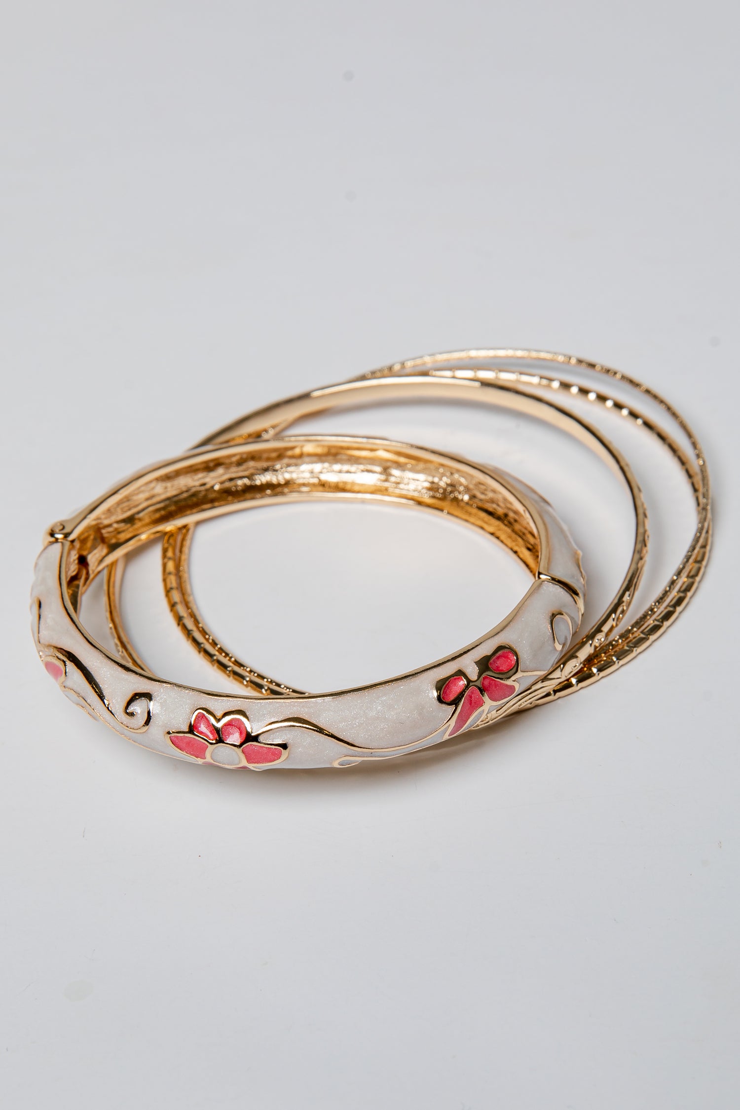 Set of gold bangles with floral designs on a light gray background