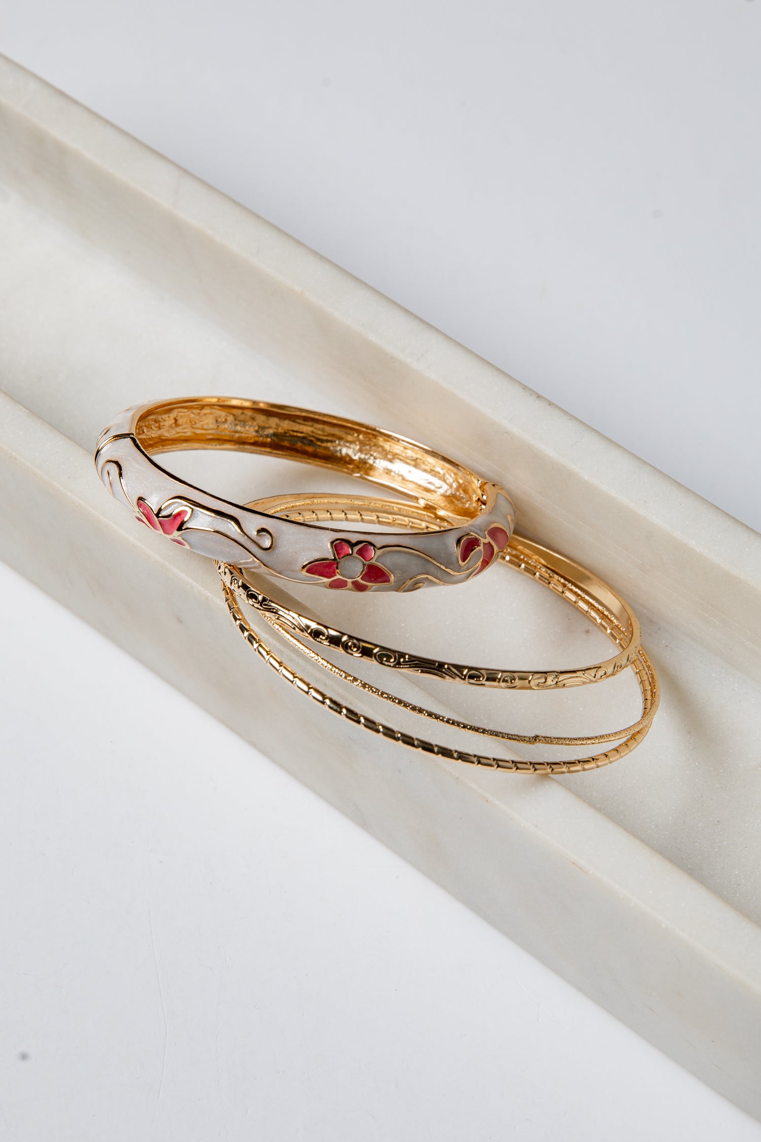 Gold bangles with floral designs on a white surface