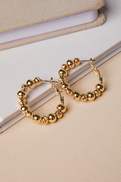 Gold hoop earrings with bead detailing on a beige surface