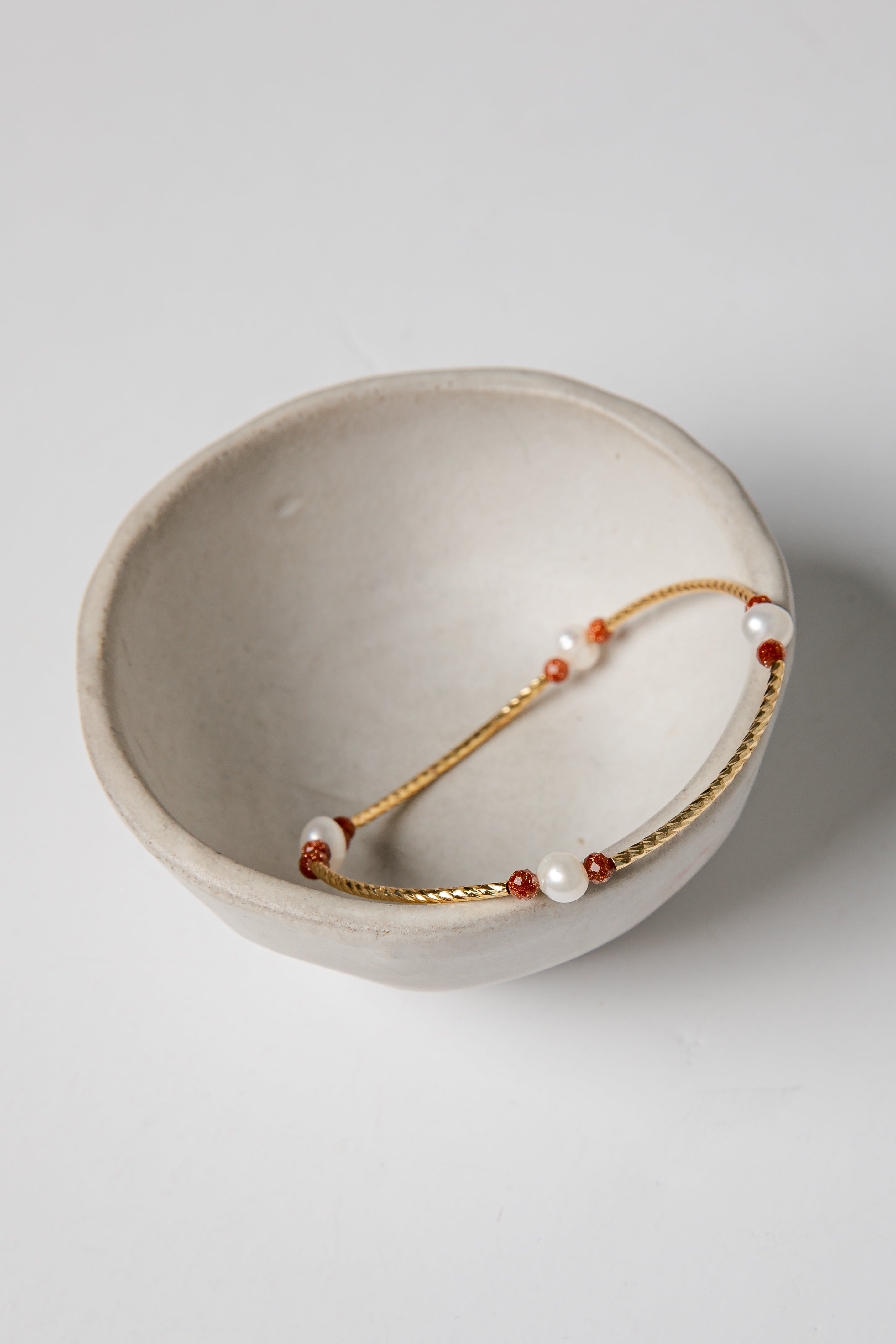 Bracelet with red and white beads on a gold chain in a beige bowl on a light gray background
