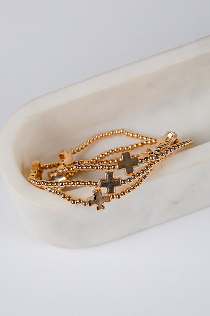 Gold chain bracelet with star and cross charms on a white dish