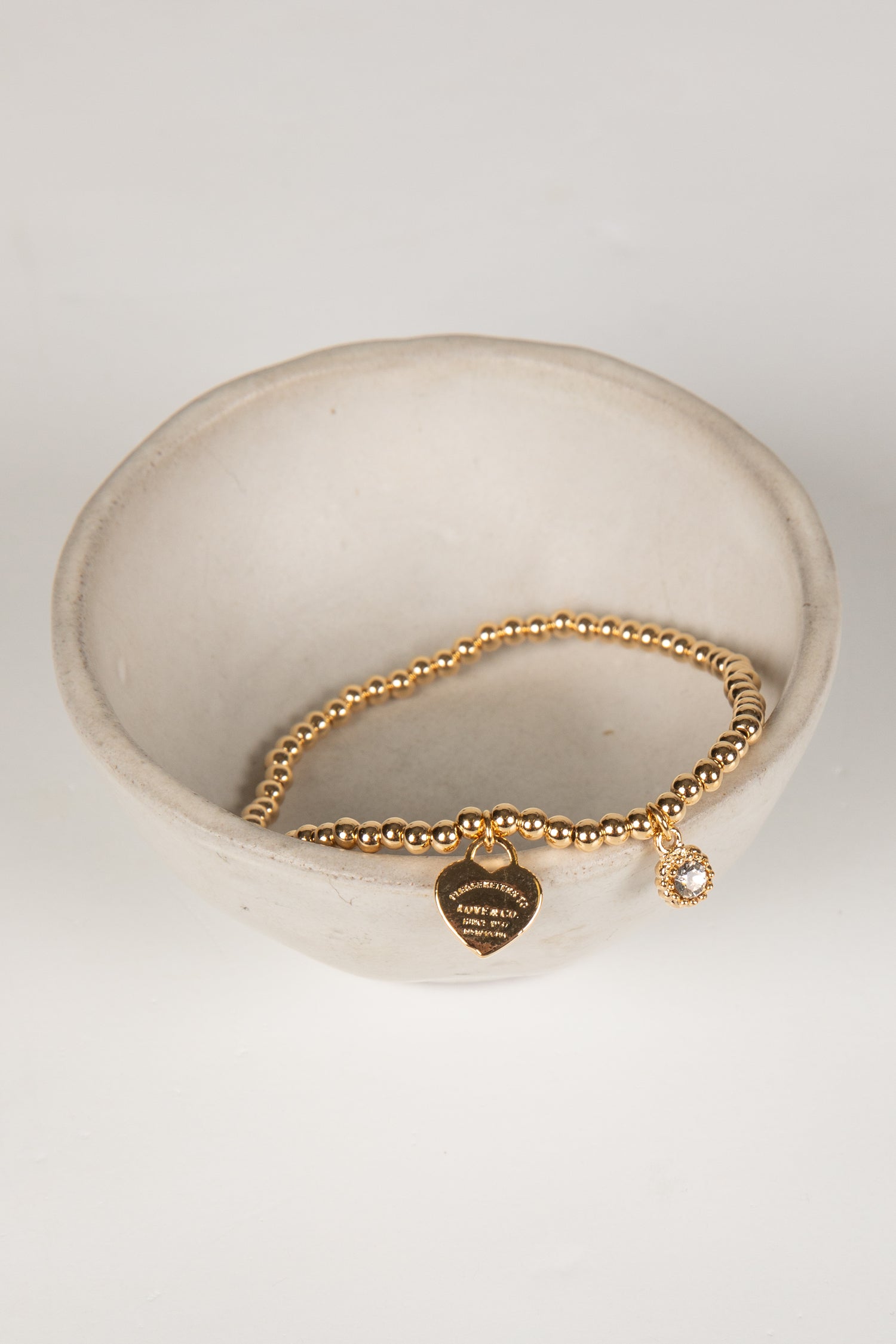 Gold bracelet with heart and round charm on a white dish
