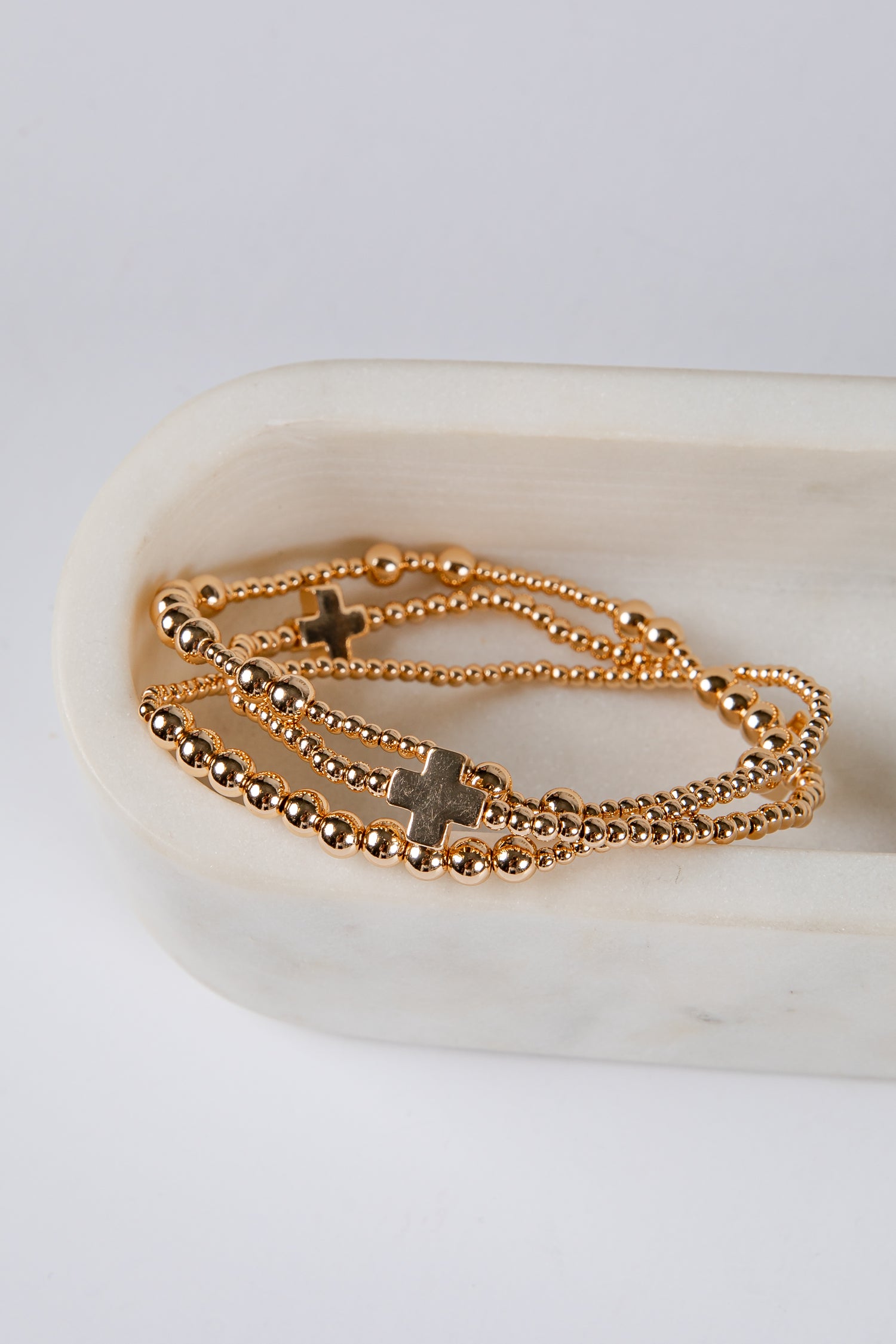 Gold chain bracelet with cross charms on a white dish