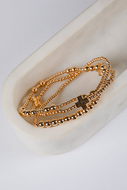 Gold beaded bracelet with cross charms on a white dish