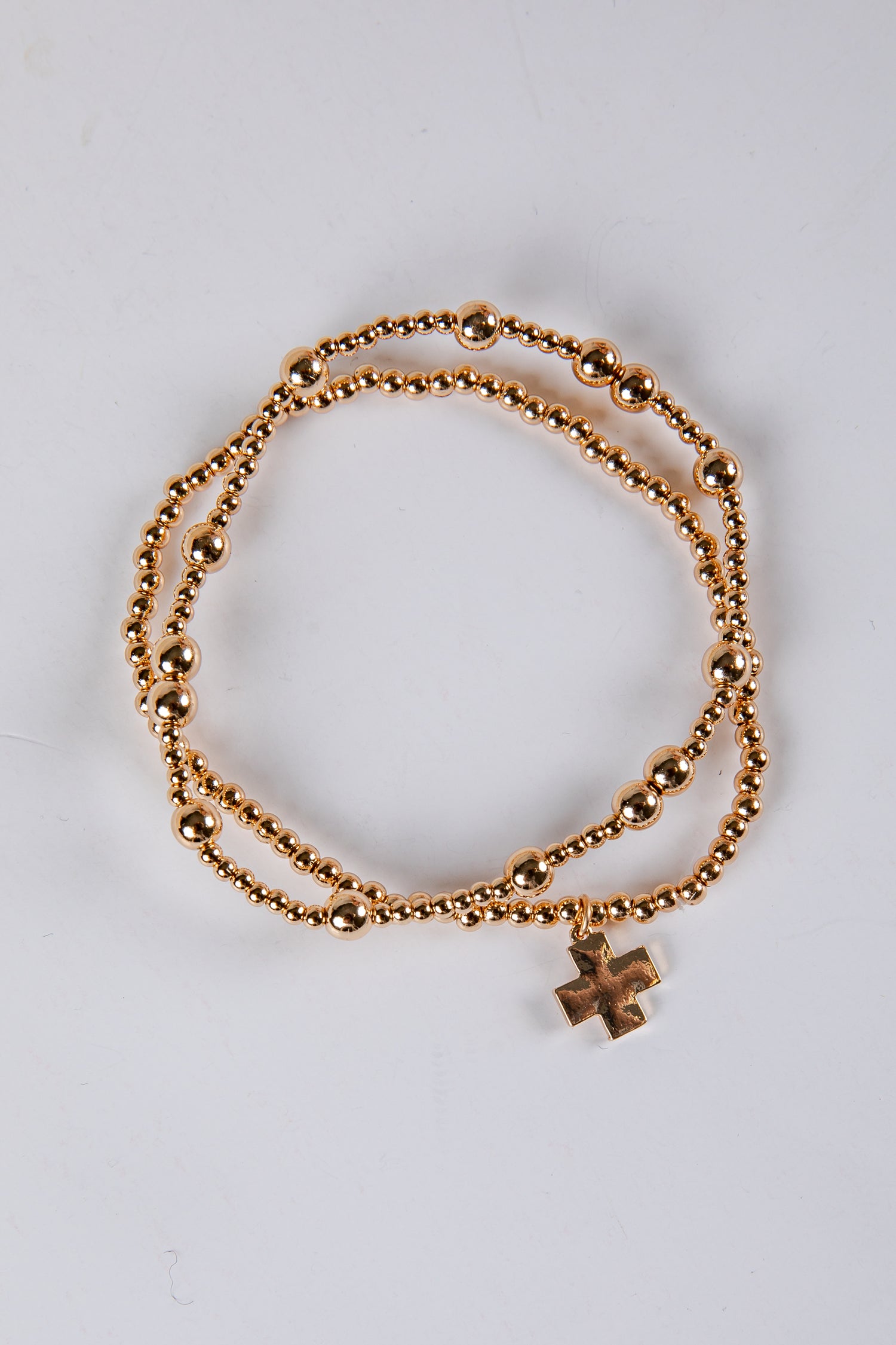 Gold bracelet with a cross charm on a light gray background