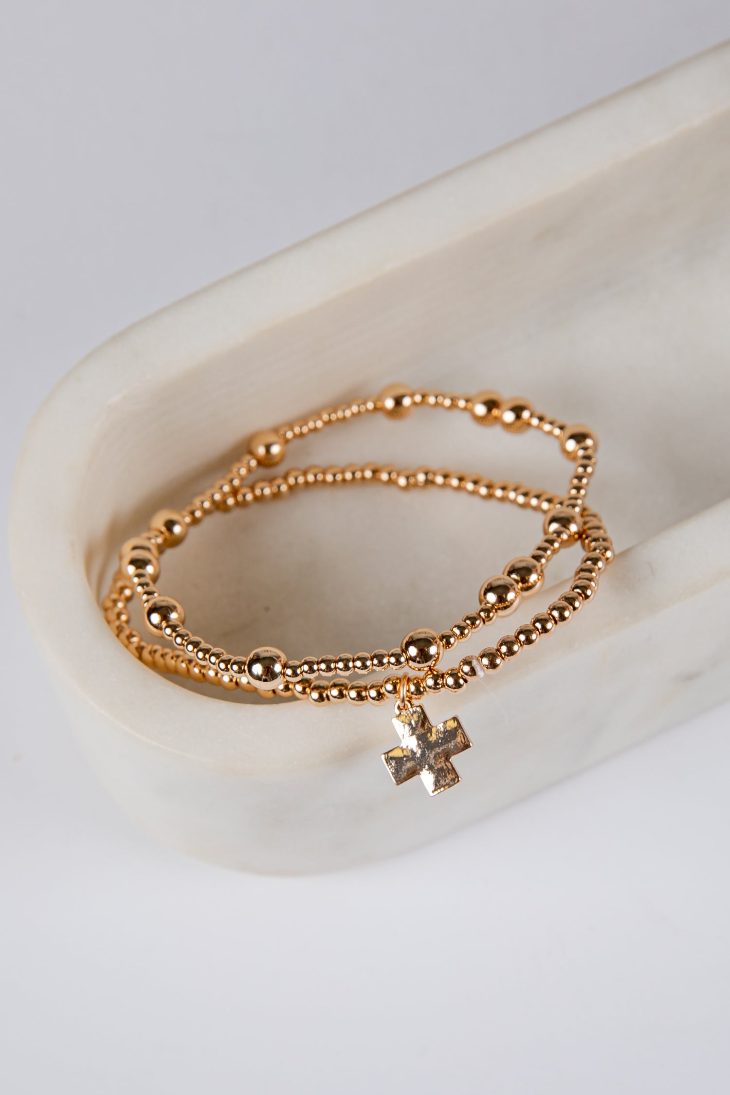 Gold bracelet with a cross charm on a white ceramic dish