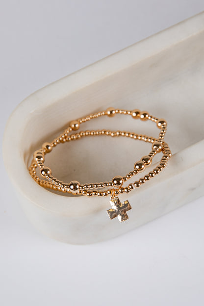 Gold bracelet with a cross charm on a white ceramic dish