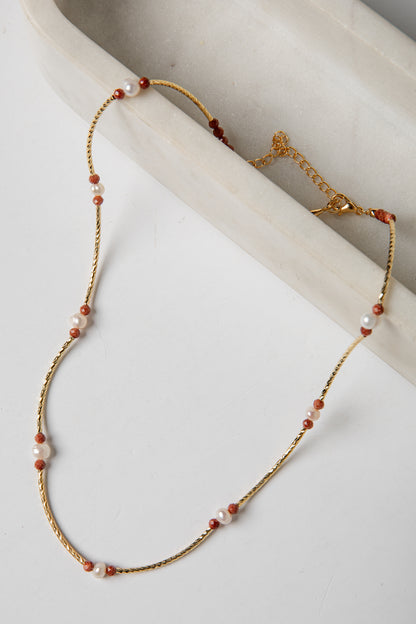 Necklace with gold chain and red and white beads on a light background