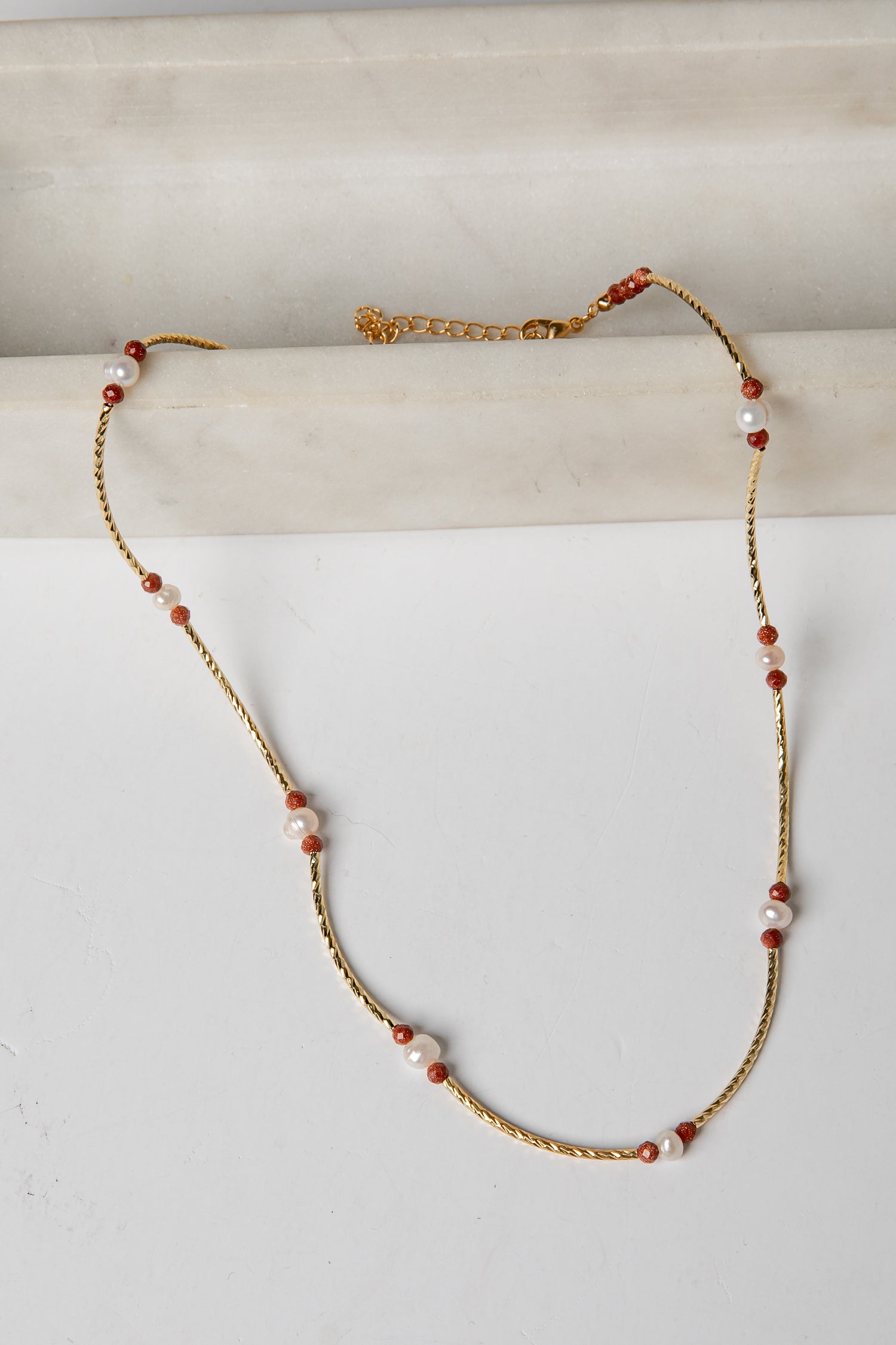 Necklace with gold chain and red and white beads on a light background