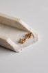 A pair of small gold bee stud earrings resting on a white ceramic tray against a light gray background.
