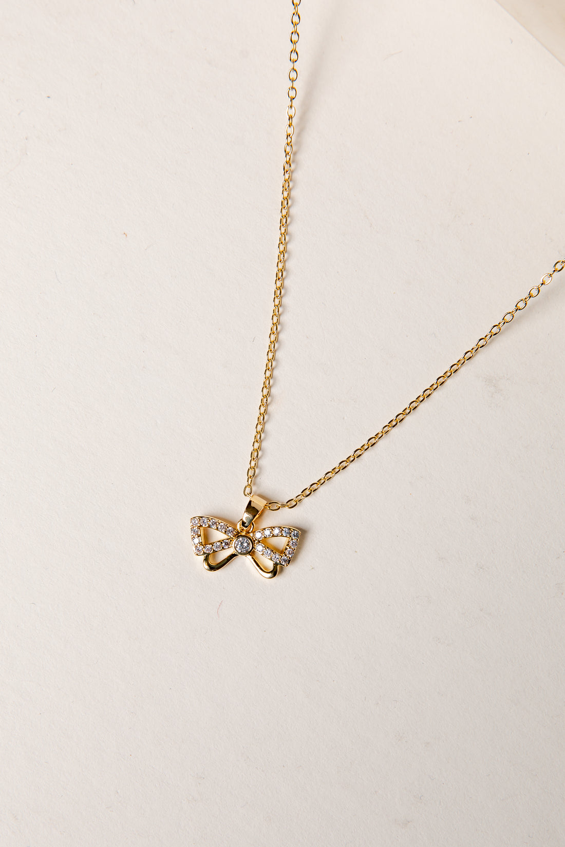 Gold necklace with a bow-shaped pendant on a light background