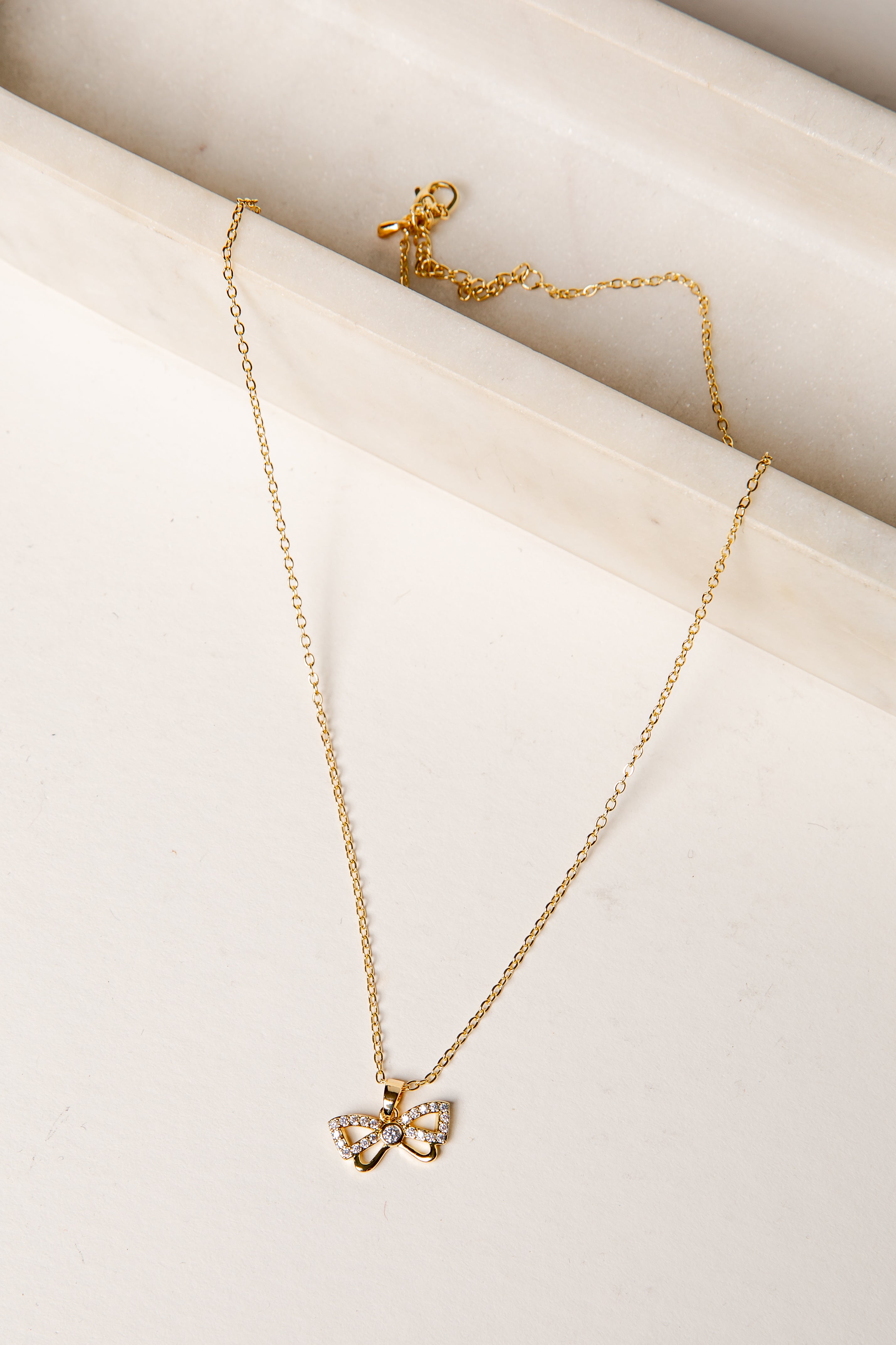 Gold necklace with a bow pendant on a light beige surface
