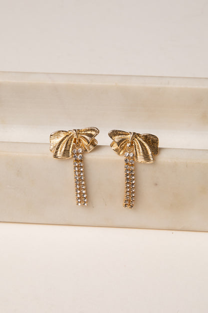 Gold bow-shaped earrings on a marble surface