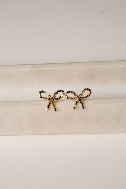 Gold bow-shaped earrings on a marble surface