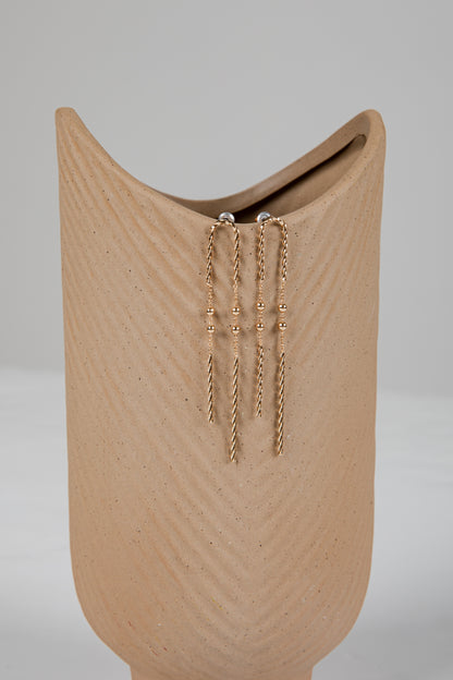 Gold chain earrings on a beige stand against a gray background